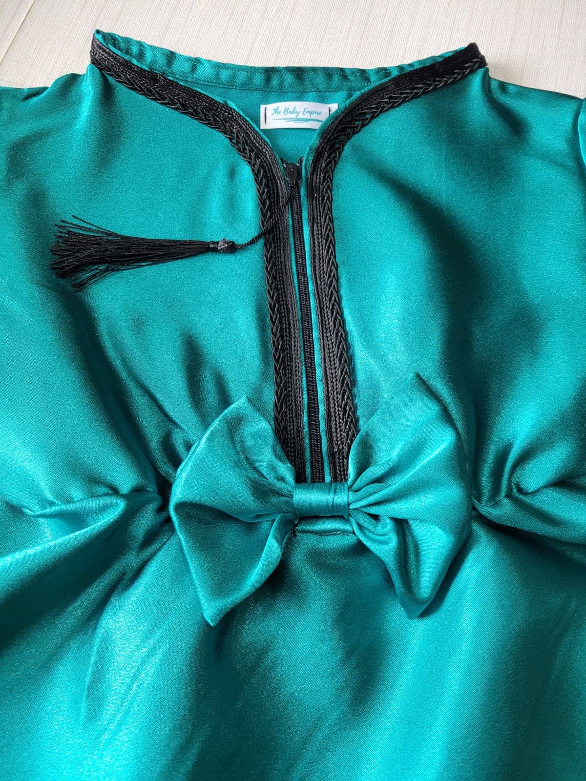 Teal dress with black trim and tassel on a light wooden surface