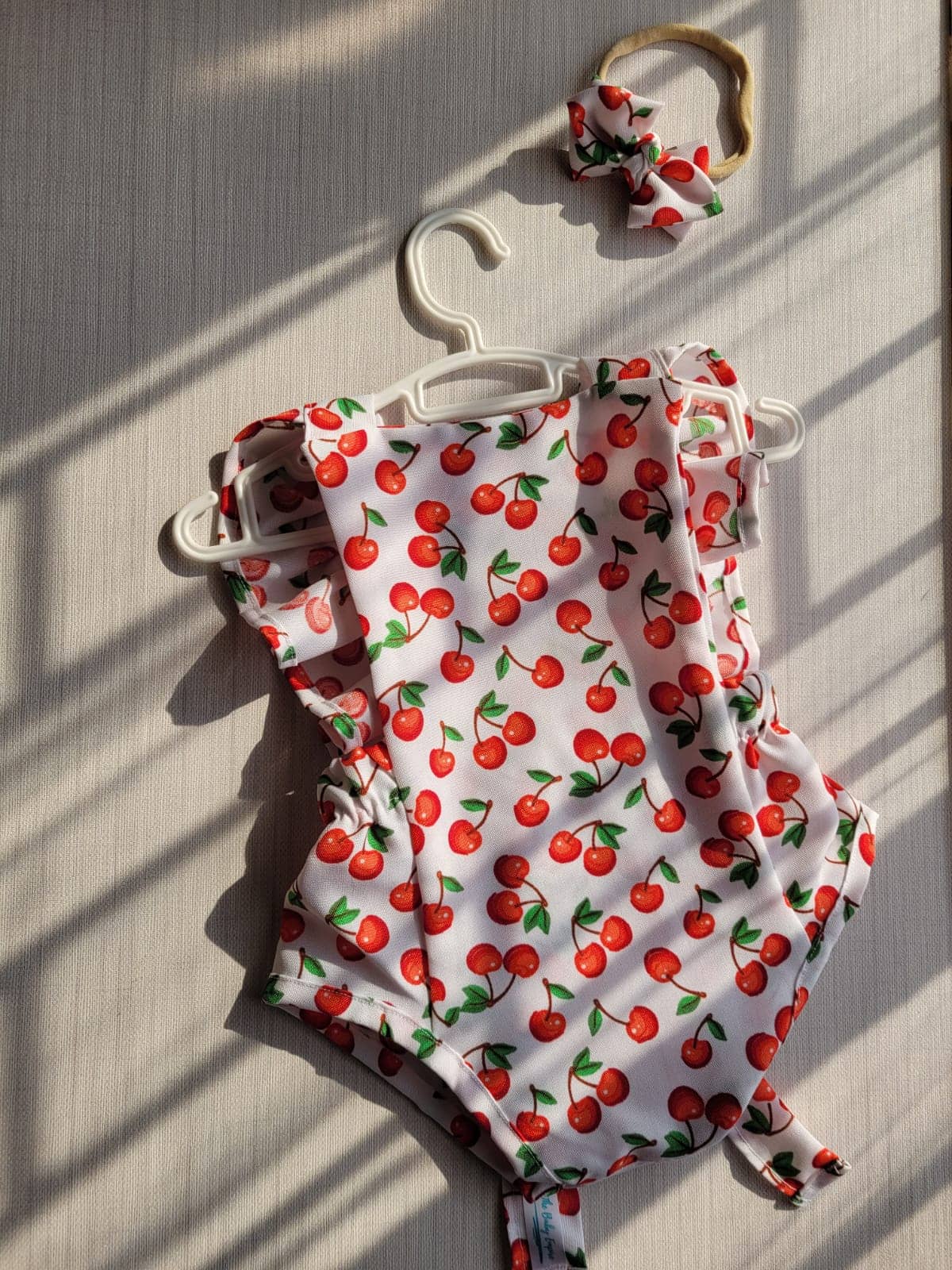 Baby romper with cherry pattern on a hanger against a wooden background