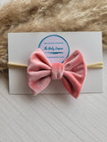 Pink velvet bow headband on a white card with 'The Baby Empire' logo, against a textured beige background.