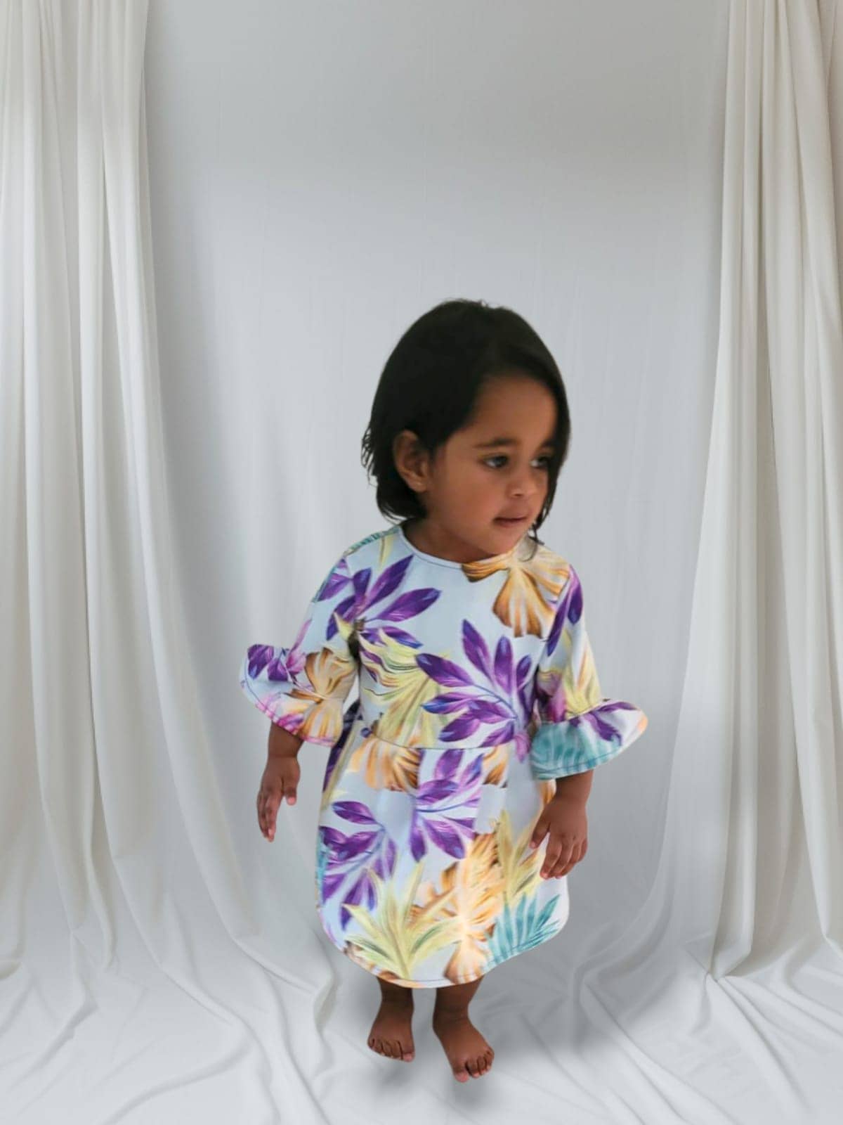 Child wearing a floral dress with purple and yellow flowers on a white background