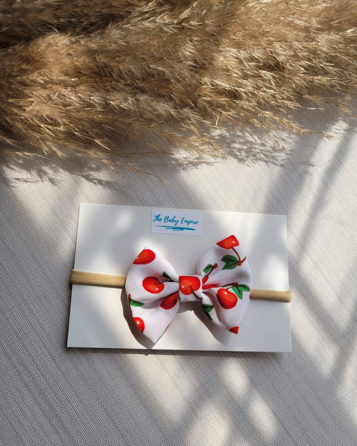 White headband with red cherries design on a white card, placed on a textured surface.