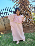 Child in a pink abaya standing outdoors with a palm tree in the background