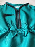 Teal dress with black trim and tassel on a light wooden surface