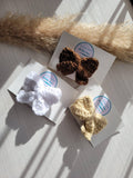 Three knitted hair bows on white cards with a decorative straw-like object in the background.