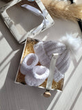 White baby booties and hat set in a decorative box on a light surface.