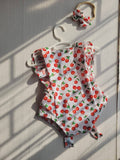 Baby romper with cherry pattern on a hanger against a neutral wall