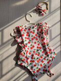 Baby romper with cherry pattern on a hanger against a wooden background