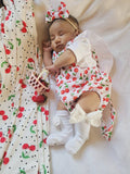 Baby in cherry-themed outfit with matching headband on a white blanket