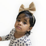 Child wearing a beige bow headband with a white background
