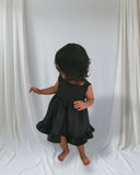 Child wearing a black dress standing against a white curtain