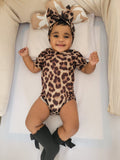 Baby wearing a leopard print outfit with a matching headband on a white surface