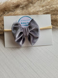 Gray velvet bow headband on a white card with a fluffy background