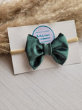 Green bow headband on a card with 'The Baby Empire' branding, placed on a textured surface.