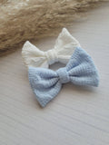 Two knitted bows, one white and one blue, on a textured surface with a blurred natural background.