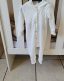 White baby onesie on a hanger in front of a white crib.