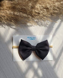 Black bow headband on a white card with 'The Baby Empire' branding, placed on a textured surface.