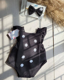 Black baby romper with white floral patterns and matching hair bow on a light surface.