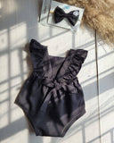 Black romper with ruffled straps and a matching hair bow on a light surface.